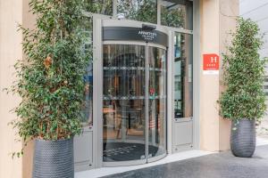 une porte tournante menant à un bâtiment avec deux plantes en pot dans l'établissement Appart'City Collection Paris Gare de Lyon, à Paris