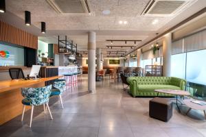un vestíbulo con un sofá verde, mesas y sillas en Hotel Bed4U Pamplona, en Cordovilla