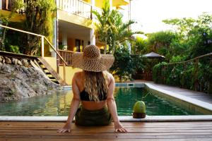 kobieta w kapeluszu siedząca obok basenu w obiekcie Villa Botanic Garden w mieście Itacaré