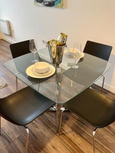 a glass table with two chairs and plates and wine glasses at Liverpool Waterfront Apartment in Liverpool