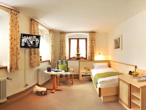 a bedroom with a bed and a table and a tv at Gästehaus Enzianhof Hotel Garni in Oberammergau