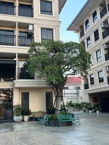 a tree in front of a building with green benches at Baan Thanakul Residences in Samutprakarn