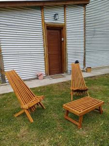 two wooden chairs and a bench in the grass at Departamento Las Maras III in El Chalten