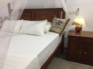 Cama con almohadas blancas y mesa con lámpara en Tropical Villa en Galle