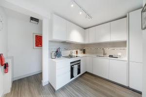 uma cozinha branca com armários brancos e pisos de madeira em Ickburgh Road Guesthouse em Londres