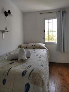 Bett in einem weißen Zimmer mit Fenster in der Unterkunft Cabaña a pasos del lago in Tandil