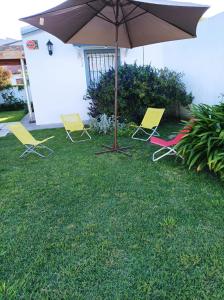 tres sillas y un paraguas en un patio en Cabaña a pasos del lago en Tandil