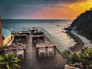 Pacific King Hotel في Cuatunalco: سطح خشبي مع طاولات وكراسي على الشاطئ