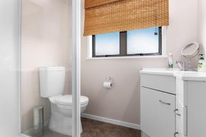 a white bathroom with a toilet and a window at The Sun Capsule - Ohope Beach Holiday Home in Ohope Beach +15 photos