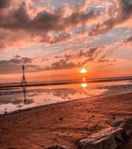 a sunset on a beach with a pole in the water at Lovely 2 bed apartment in Crosby in Liverpool