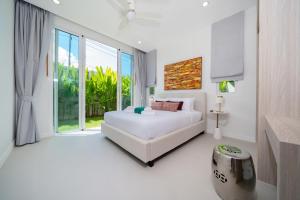 a white bedroom with a bed and a large window at Peykaa Estate Pool Villa by HCR in Phuket Town