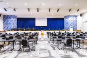 Großes Zimmer mit Tischen, Stühlen und einem Bildschirm in der Unterkunft Bernstein Salzlandcenter in Staßfurt