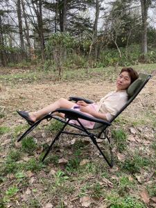 une femme assise sur une chaise de jardin dans un champ dans l'établissement 西神楽の杜, à Nishi-kagura