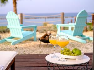 Dois copos de vinho e uma taça de fruta numa mesa com cadeiras. em Kyma I - Beachfront Residence At Latsi em Pólis