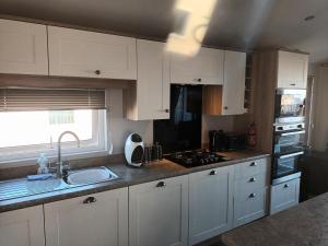 a kitchen with white cabinets and a sink and a window at Beautiful 4 Berth Lodge With Free Wifi At Pakefield Holiday Park Ref 68019cr in Lowestoft