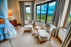 een slaapkamer met een bed en 2 stoelen en ramen bij Hitgeheim Country Lodge in Addo