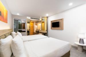 a white bedroom with two beds and a tv at Clarian Hotel Beach Patong in Patong Beach
