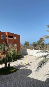 un bâtiment sur une plage avec des palmiers et un trottoir dans l'établissement Appartement T3 proche de la Plage !, à Jāmi‘ al Guelloufi