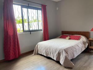 1 dormitorio con 1 cama con cortinas rojas y ventana en Villa vue 1 C.A.M, en Albion