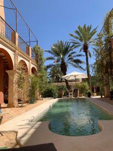 a swimming pool in front of a building with palm trees at RIAD CHANT D'ETOILES tadighoust in El Hara