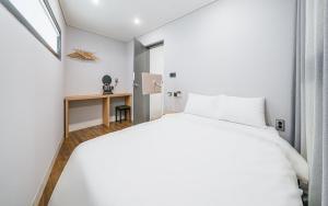1 dormitorio con cama blanca y escritorio en Aroomi Hotel Hyupjae en Jeju