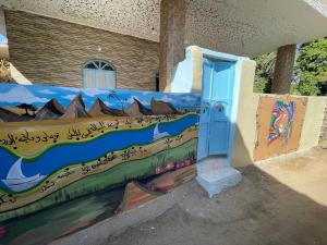 a wall with a painting on it with a blue door at Shater Nubian House in Aswan
