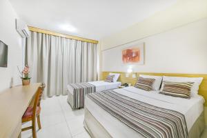 a hotel room with two beds and a desk at Hotel Nacional Inn Piracicaba in Piracicaba