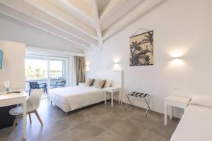 Cette chambre blanche comprend un lit et une table. dans l'établissement Hotel S'arena Beach, à La Caletta