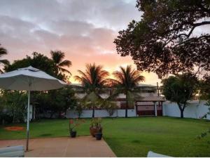 a house with an umbrella and a lawn with palm trees at Casa de praia por temporada. in Camacari