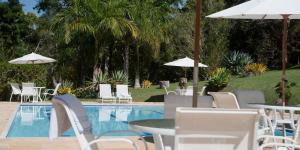 a pool with white chairs and tables and umbrellas at Pousada Les Roches in Itaipava