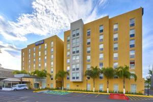 a yellow building with palm trees in a parking lot at City Express by Marriott Queretaro Jurica in Quer&eacute;taro