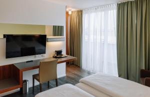 a hotel room with a bed and a desk with a television at HEINhotel vienna airport in Schwechat