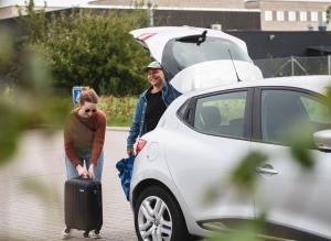 Un uomo e una donna che passano davanti a un'auto con i bagagli di Hotel GUESTapart a Arhus