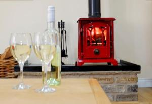 dos copas de vino sentadas en una mesa frente a una estufa en The Ash Cottage, en Brecon