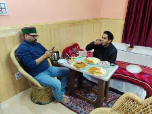 two men are sitting at a table with food at Crimson inn b&b in Rāmpur