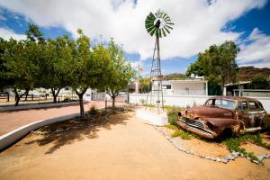an old rusty car parked next to a windmill at Kleinplasie Guesthouse in Springbok