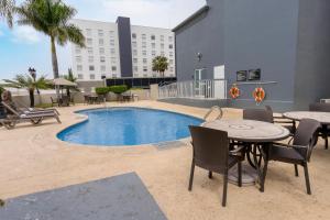 une terrasse avec une table, des chaises et une piscine dans l'établissement Hampton Inn by Hilton Guadalajara-Aeropuerto, à Guadalajara