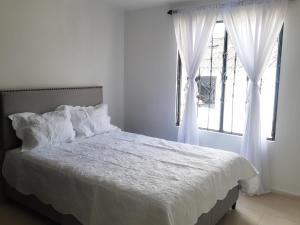 um quarto com uma cama com lençóis brancos e uma janela em Quintas de las Acacias Villavicencio em Villavicencio