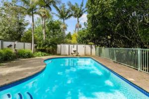 a blue swimming pool with a fence and trees at Nature Serenity Getaway with pool - deck - gardens in Auckland