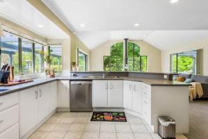 una cocina con armarios blancos, fregadero y ventanas en Nature Serenity Getaway with pool - deck - gardens en Auckland
