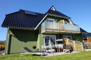 a green house with a balcony and a table and chairs at Ferienwohnung de Windroos in Born