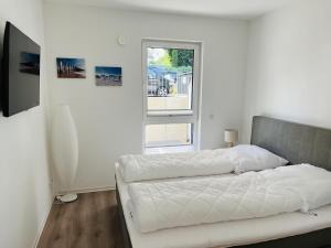 a white bedroom with a bed and a window at OceanHome in Scharbeutz