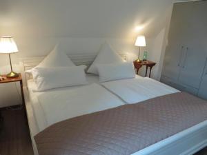 Bett mit weißer Bettwäsche und Kissen in einem Zimmer in der Unterkunft Schicke FeWo Johanna an der Nordsee Dachterrasse in Lütetsburg