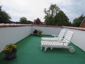zwei weiße Stühle und eine Bank auf einer Terrasse in der Unterkunft Schicke FeWo Johanna an der Nordsee Dachterrasse in Lütetsburg