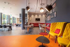 a waiting room with yellow and red chairs and tables at Campanile Berlin Brandenburg Airport in Schönefeld