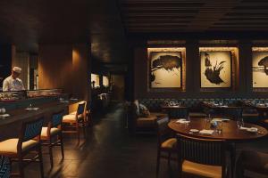 a restaurant with tables and chairs and a man standing at a counter at Nobu Hotel San Sebastián in Donostia-San Sebastián