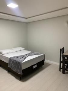 uma cama num quarto branco com uma mesa em Pousada vale do paraíso em Navegantes