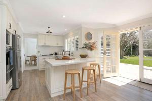 a kitchen with white cabinets and a counter with stools at Avonlea, Bowral, Southern Highlands in Bowral