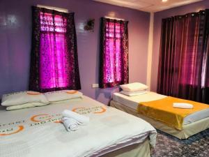 two beds in a room with purple walls and windows at Kurau Stone Chalet in Taiping