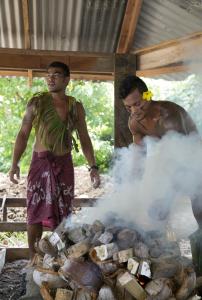 dos hombres están cocinando en una parrilla con humo en Coconuts Beach Club Resort and Spa, en Fausaga